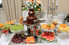 Stół z owocami (arbuzy, pomarańcze, winogrona, truskawki) i czekoladowa fontanną.
