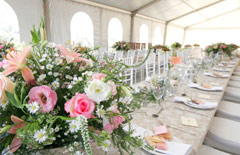 Długi stół weselny przybrany na biało z dużymi dekoracjami kwiatowymi.
